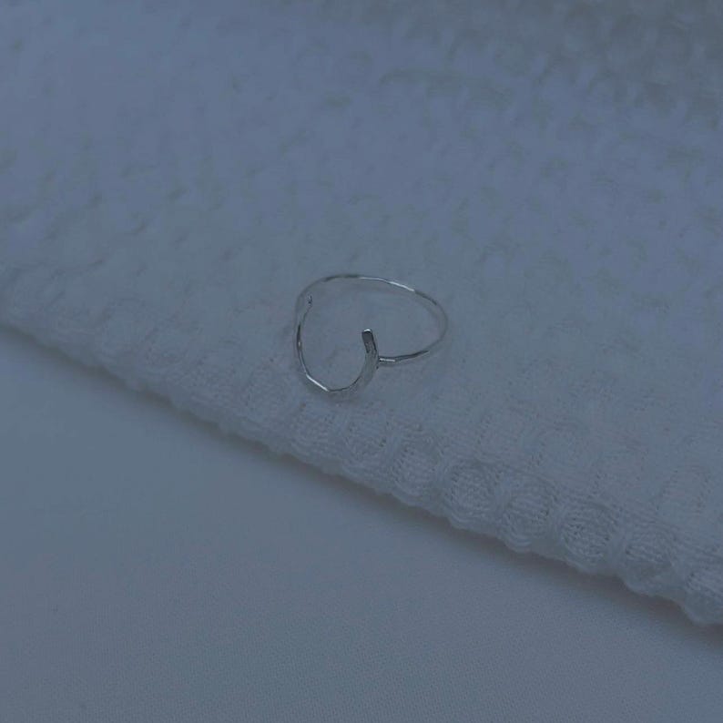 K&ouml;nnte beinhalten: Ein silberner Ring mit geometrischem Design. Der Ring ist an einer Seite offen und hat eine leicht gebogene Form.