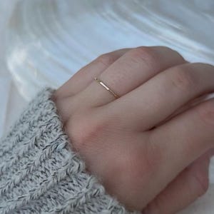 May include: A simple gold band ring worn on a finger.