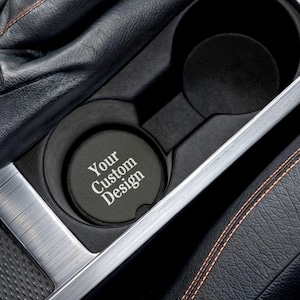 May include: A black car cup holder with a round, black coaster that says "Your Custom Design" in white text.