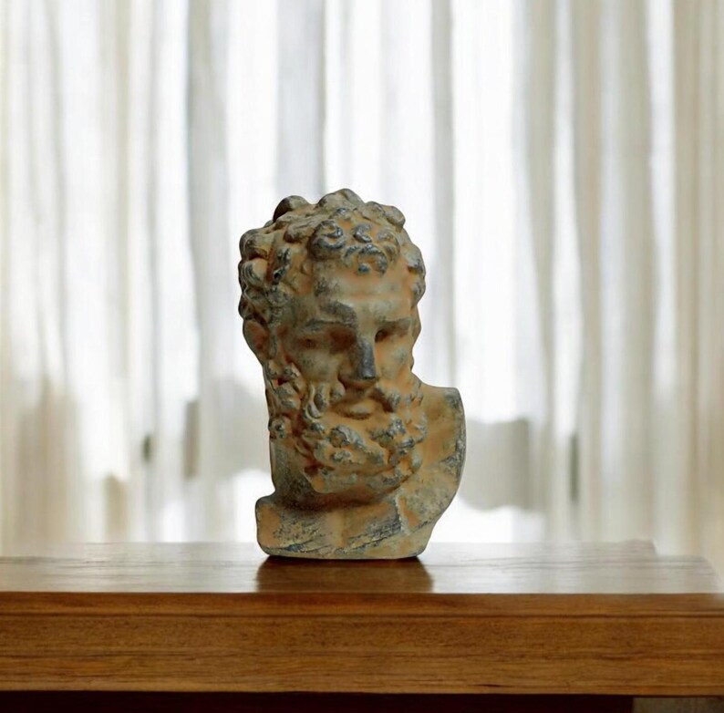 May include: A weathered gray and brown stone bust of a man with a beard. The bust is on a wooden surface.
