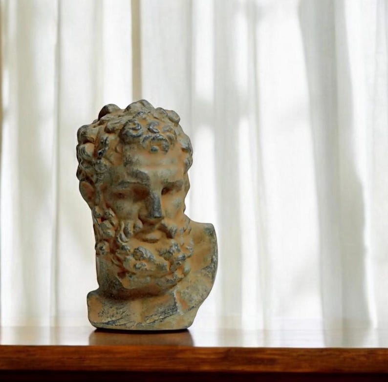 May include: A weathered gray and brown bust sculpture of a man with a beard. The sculpture is made of a rough material and has a detailed face.