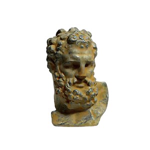 May include: A small, weathered, yellow-brown bust of a man with a beard. The bust is made of a rough, textured material and has a detailed face.