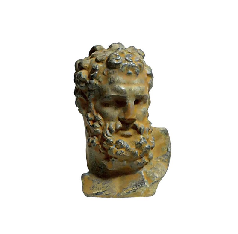 May include: A small, weathered, yellow-brown bust of a man with a beard. The bust is made of a rough, textured material and has a detailed face.