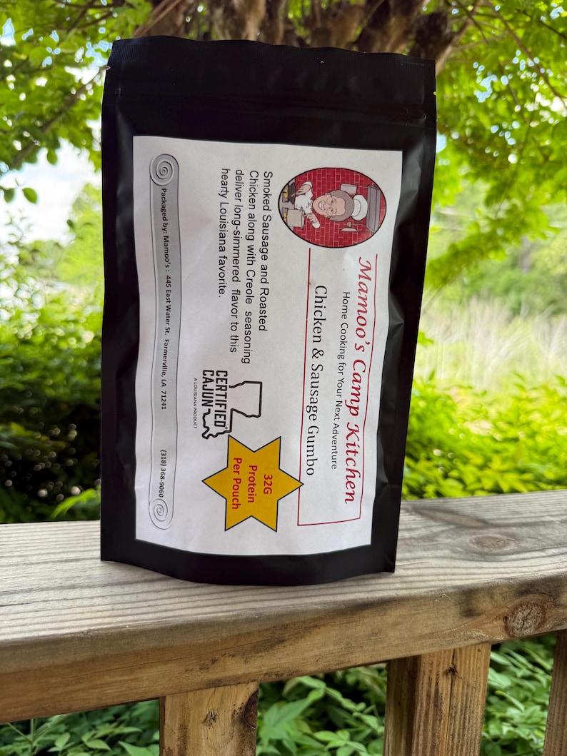 May include: A black pouch of Mamoo's Camp Kitchen Chicken & Sausage Gumbo. The label features text including "Smoked Sausage and Roasted Chicken" and "32G Protein Per Pouch." The product is certified Cajun and packaged in Farmerville, LA.