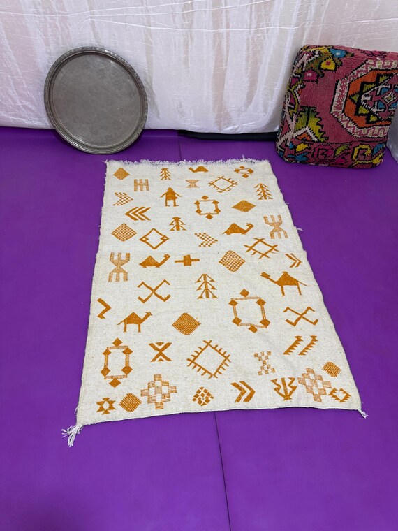 Handwoven Moroccan rug with traditional Amazigh symbols in saffron thread on natural wool – tribal and cultural artisan home decor.