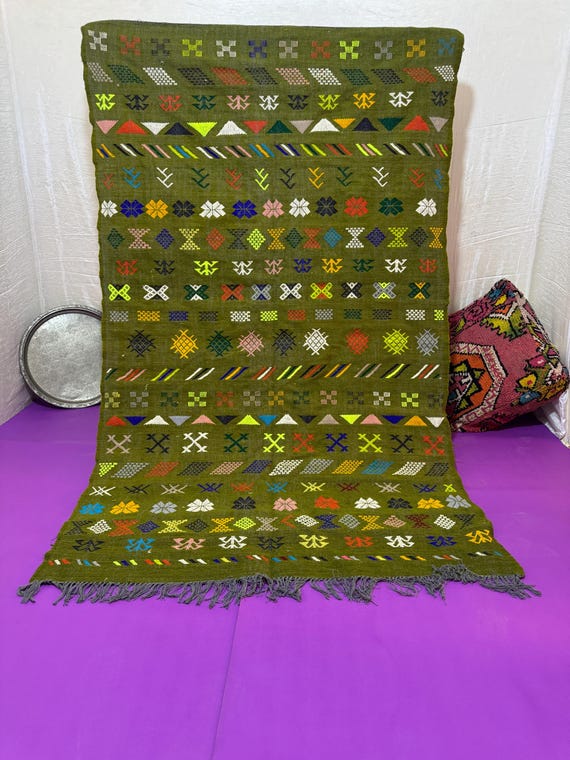Amazigh carpet with traditional motifs and bright colors on an olive green background, reflecting the charm of authenticity and high