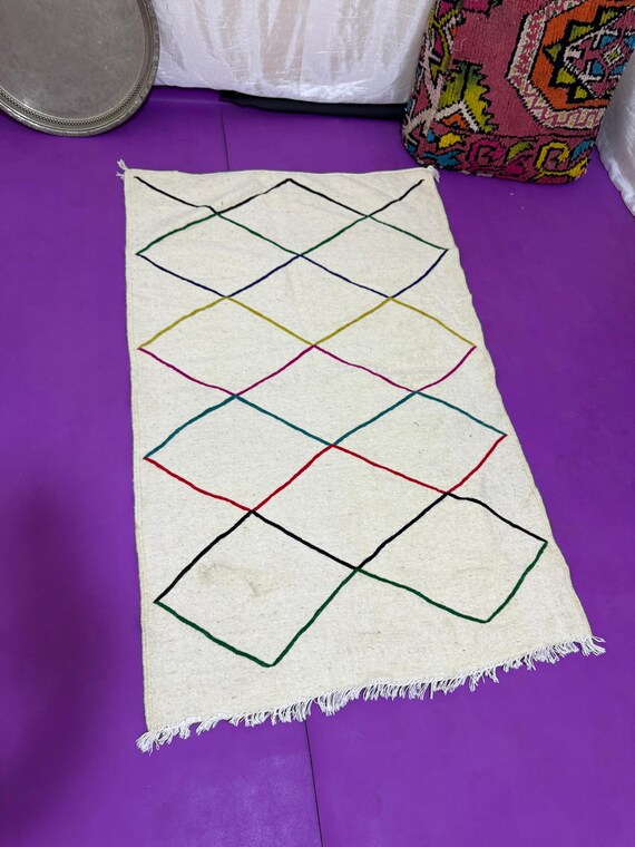 Handwoven Moroccan rug with colorful intersecting lines on natural wool – minimalist Berber design blending tradition with modern style.