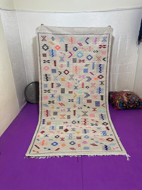 A natural ivory Berber rug decorated with colorful traditional symbols, carefully handwoven to create an authentic Moroccan artistic touch.