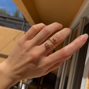 Op de afbeelding: Een gouden ring met twee roze parel accenten. De ring is om een vinger gewikkeld.