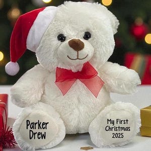 May include: A white plush teddy bear wearing a red and white Santa hat and a red bow. The bear's paw has the text "Parker Drew" and the other paw has the text "My First Christmas 2025".