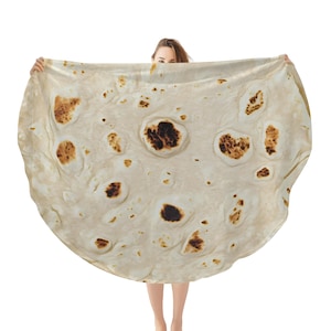 Op de afbeelding: Een groot, rond, beige tortilla-deken met bruine vlekken. Het deken wordt vastgehouden door een persoon, die alleen zichtbaar is vanaf de taille.