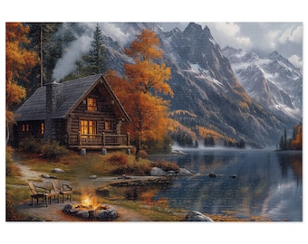 May include: A wooden cabin with a porch light on sits on the edge of a lake in the mountains. The lake is surrounded by trees with fall foliage. A campfire burns in front of the cabin with two chairs nearby.