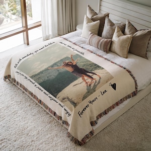 May include: A woven tapestry throw blanket with a photo of a couple standing on a cliff with their arms outstretched. The blanket has a fringe border and the text "life with somebody, you want the life to start as soon as possible. When you realize you want to spend the rest of your  Forever Yours - Lea" is printed on the blanket.