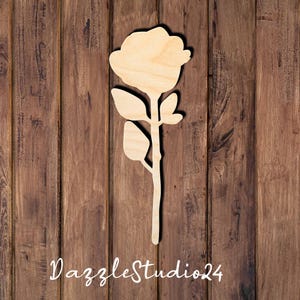 May include: A flat, laser-cut wooden cutout in the shape of a single rose flower with a stem and three leaves. The natural light-colored wood grain is visible on the surface. The text DazzleStudio24 is printed in white at the bottom of the image.