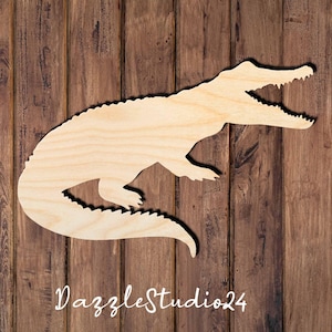 May include: A wooden cutout of an alligator with an open mouth. The cutout is made of light brown wood and is approximately 10 inches long.