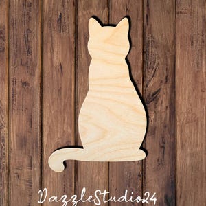 May include: A light-colored, unfinished wooden cutout in the shape of a sitting cat with its tail curled to the side. The surface displays a natural wood grain pattern, and the silhouette features pointed ears and a smooth, rounded body contour.