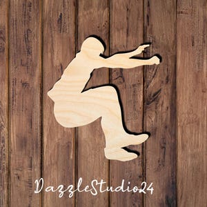 May include: A wooden cutout of a person in a jumping pose. The cutout is light brown and has a smooth, unfinished surface.