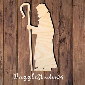 May include: Wooden cutout of a shepherd with a staff, standing against a woodgrain background. The shepherd is facing left and has a beard. The staff has a curved top.