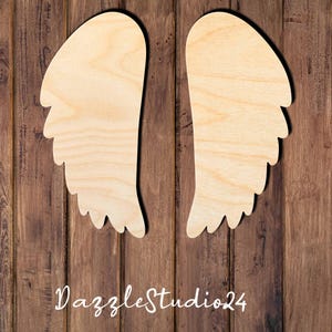 May include: Two unfinished wooden angel wings with a scalloped edge. The wings are on a brown wood background.