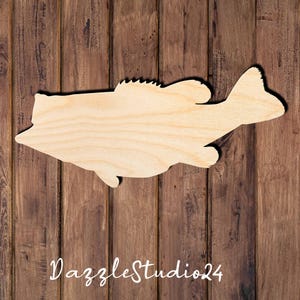 May include: A light-colored, unfinished wooden cutout shaped like a largemouth bass fish. The cutout features a smooth, flat surface with visible natural wood grain patterns, a distinct dorsal fin, a tail fin, and pectoral fins in a side profile.