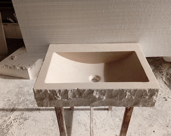 May include: A white stone bathroom sink with a rough, textured edge. The sink is mounted on a stand with three legs.