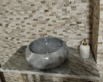 May include: A gray marble sink bowl with a white marble countertop and a white soap dispenser with a gold pump.