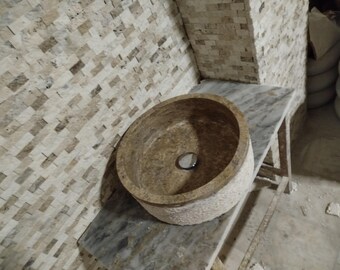May include: A round, brown stone sink with a textured surface. The sink is set into a white marble countertop.