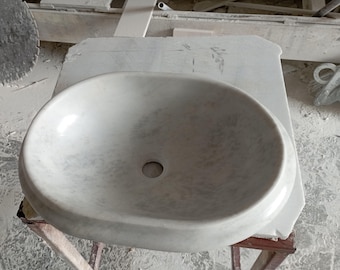 May include: A white marble bathroom sink with a smooth, oval-shaped basin. The sink is sitting on a wooden stand.