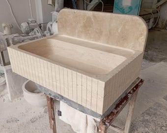 May include: A white stone sink with a backsplash, made of a textured material. The sink is sitting on a wooden stand.