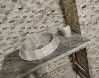 May include: A white marble bathroom sink with a round, bowl-shaped basin sits on a marble countertop with a white ceramic soap dispenser with a gold pump.