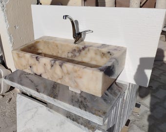 May include: A white marble sink with a chrome faucet. The sink is rectangular and has a smooth, polished surface. The faucet is mounted on the wall and has a single handle.