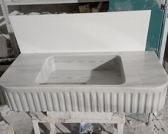 May include: A white marble bathroom sink with a rectangular basin and a fluted base.
