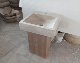 May include: A white stone pedestal sink with a rectangular basin and a brown wooden base.
