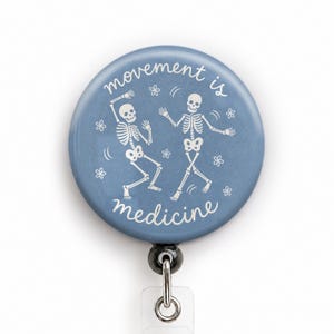 May include: A circular blue badge reel featuring a white graphic of two dancing skeletons surrounded by small flower icons. The text "movement is medicine" is printed in white script lettering around the skeletons on the blue background.