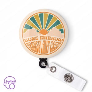 May include: A white button with a retro-style sunburst design and the text "BONE MARROW TRANSPLANT CREW" in orange. The button is attached to a black retractable badge reel with a white strap.
