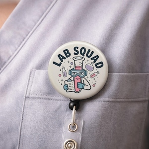 May include: A round, white badge reel with the words "LAB SQUAD" in black. The badge reel features a cartoon illustration of a test tube wearing goggles and holding a clipboard. The reel is attached to a clear plastic holder.