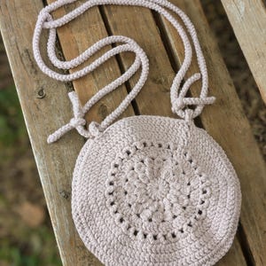 May include: A light purple crocheted bag with a circular design and a long strap.