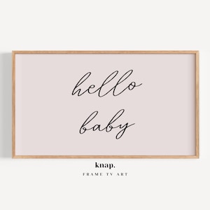 May include: A framed print with a light pink background and black text that reads "hello baby". The frame is a light wood color. The bottom of the print has the text "knap. FRAME TV ART".