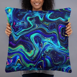 Puede incluir: Una almohada decorativa con un patrón abstracto de espiral azul, verde y amarillo sobre un fondo negro. El patrón se asemeja a líquido girando en el espacio.