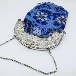 May include: An antique beaded purse with a silver frame and chain. The purse features a blue beaded design with white floral patterns. The silver frame is intricately carved with floral and scroll designs, and the chain is a delicate silver link.