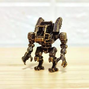 May include: A miniature bronze-coloured mechanical robot figurine featuring a detailed armoured torso, articulated limbs with clawed hands, and a prominent cage-like structure on the front. The figure displays the number 03 on its shoulder.