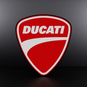 May include: A red and white logo featuring the word "DUCATI" in white lettering. The logo is shaped like a shield with a curved line across the top.