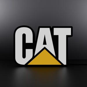 Puede incluir: Un logotipo en blanco y negro con la palabra "CAT" en letras blancas con un triángulo amarillo detrás de la "A".