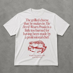 May include: White t-shirt with red text and a graphic of a grilled cheese sandwich. The text reads, "The grilled cheese that he makes in The Devil Wears Prada is a little too burned for having been made by a professional chef."