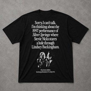 May include: A black short-sleeved t-shirt featuring white text that reads: Sorry, I can't talk. I'm thinking about the 1997 performance of Silver Springs where Stevie Nicks stares a hole through Lindsey Buckingham. Below is a graphic and the text: It is, in my opinion, the best performance of a song ever.