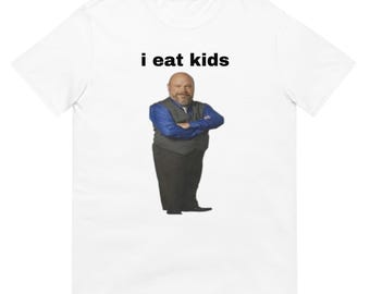 May include: White t-shirt with the text "i eat kids" in black font above an image of a man in a blue shirt, gray vest, and black pants with his arms crossed.