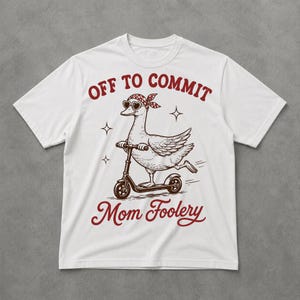 May include: White t-shirt featuring a cartoon goose riding a scooter. The goose wears heart-shaped sunglasses and a bandana. Text on the shirt reads "OFF TO COMMIT Mom Foolery" in red script.