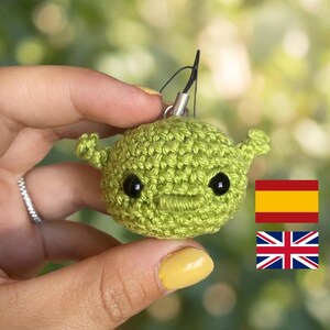 Puede incluir: Un pequeño dije de ganchillo de color verde claro, de forma redonda, con dos orejas prominentes y dos ojos de cuentas de plástico negro. La figura de hilo hecha a mano tiene una boca plana bordada y un cordón negro con una argolla de metal.