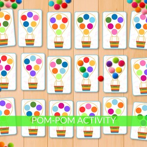 Peut inclure: Ensemble de cartes colorées avec des illustrations de montgolfières et des points de couleurs variées. Les cartes sont conçues pour une activité pompon, avec le texte "POM-POM ACTIVITY" en bas. Des pompons multicolores sont dispersés autour des cartes.