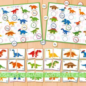 May include: Educational dinosaur-themed alphabet and puzzle activity set. Includes two matching letter boards with colorful dinosaur illustrations, plus puzzle pieces. The text reads "DINOSAURS ALPHABET AND PUZZLE ACTIVITY".